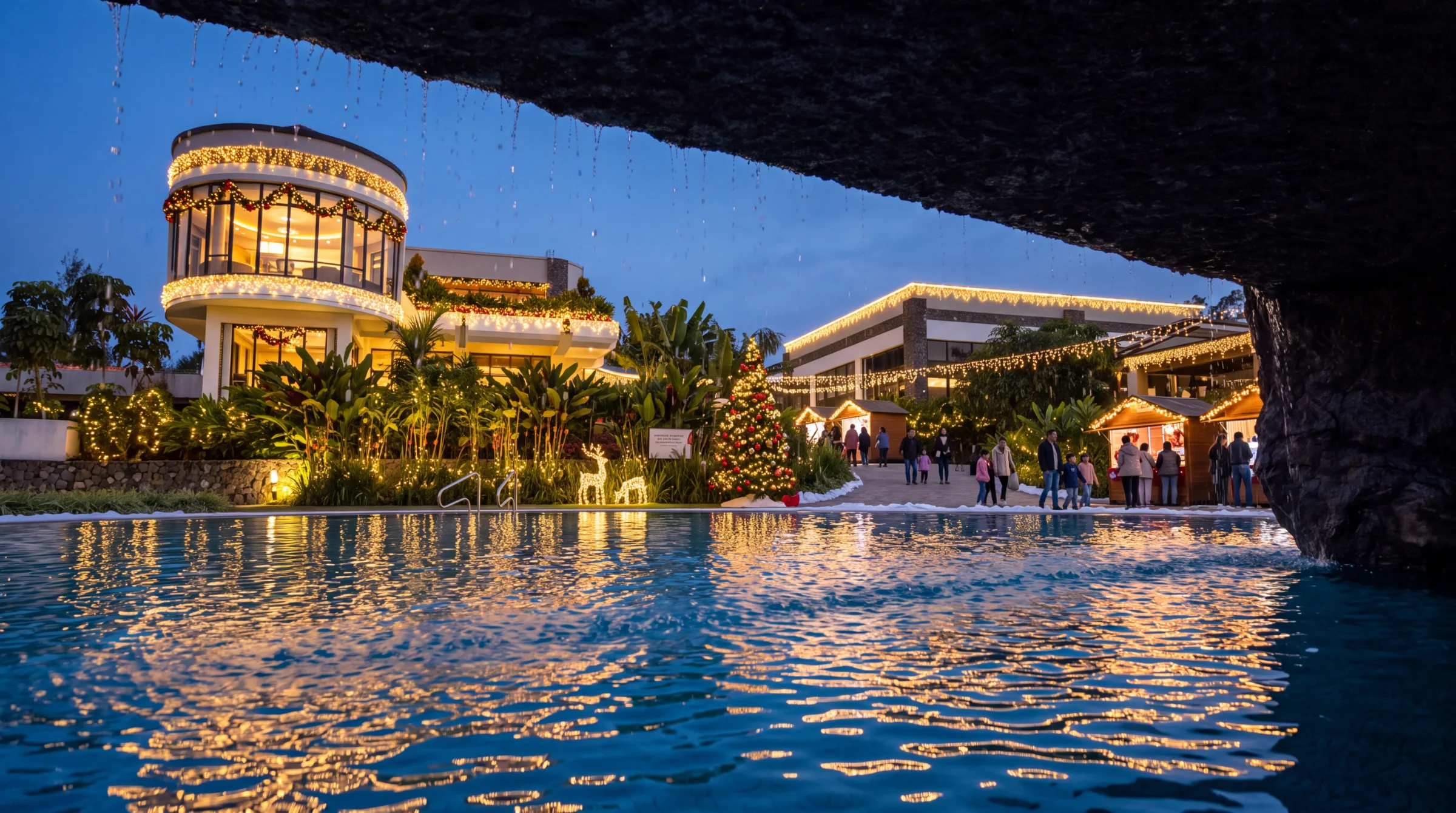 Grotta Resort's round tower and terraces dressed in garlands and warm lights at blue hour, seen from beneath the pool waterfall, with a Christmas tree and market chalets beyond