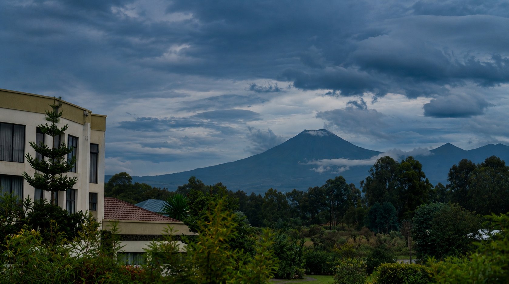 A volcano rising above the Musanze highlands under a broken cloud sky